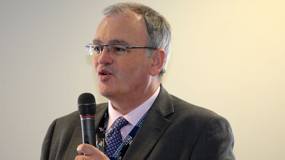 A close up of Richard wearing a suit and speaking into a microphone.